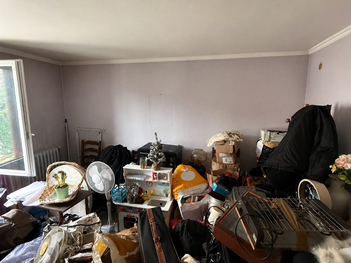 Chambre avant intervention : cartons, valises, meubles et objets empilés sur toute la surface de la pièce.